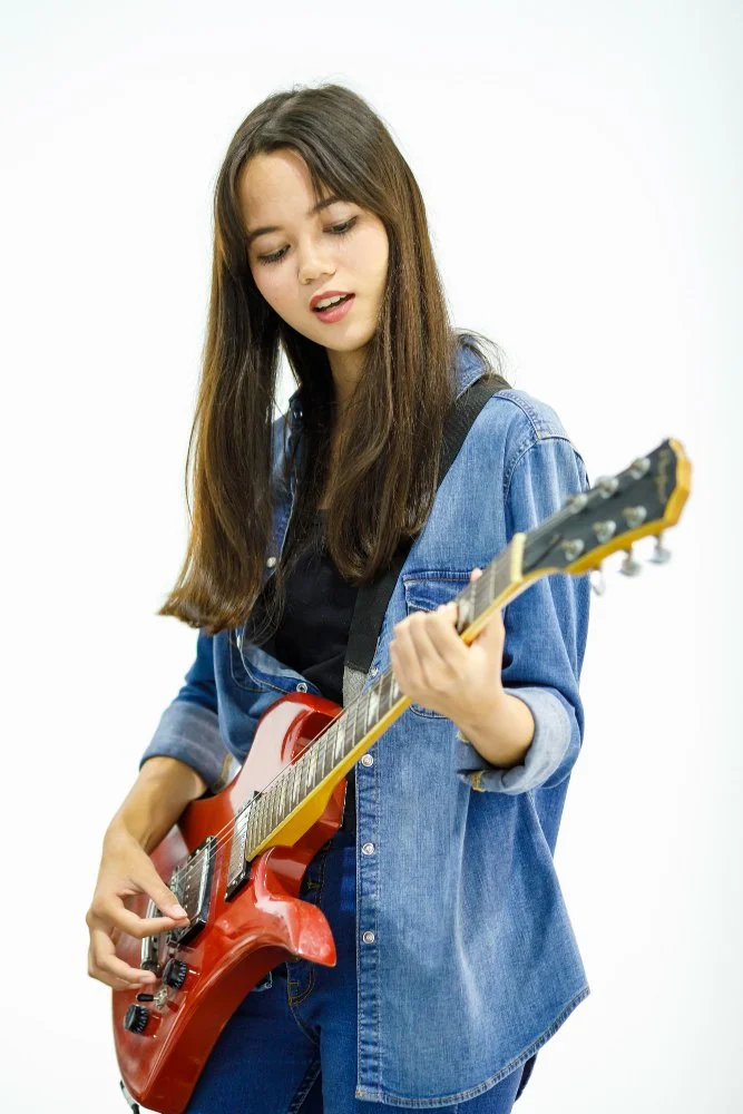 Young woman with long brown hair playing red electric guitar against a white background for Sunnyside Homeschooling's StarJam Homeschool Music Program