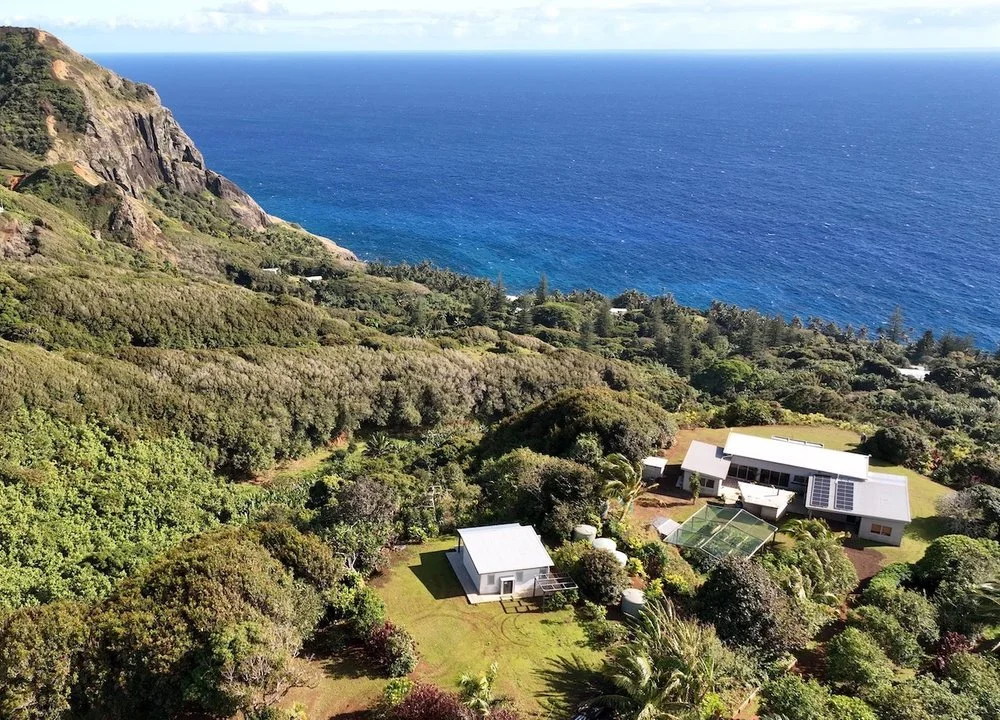 Aerial view of a coastal house surrounded by lush greenery near a cliff and ocean