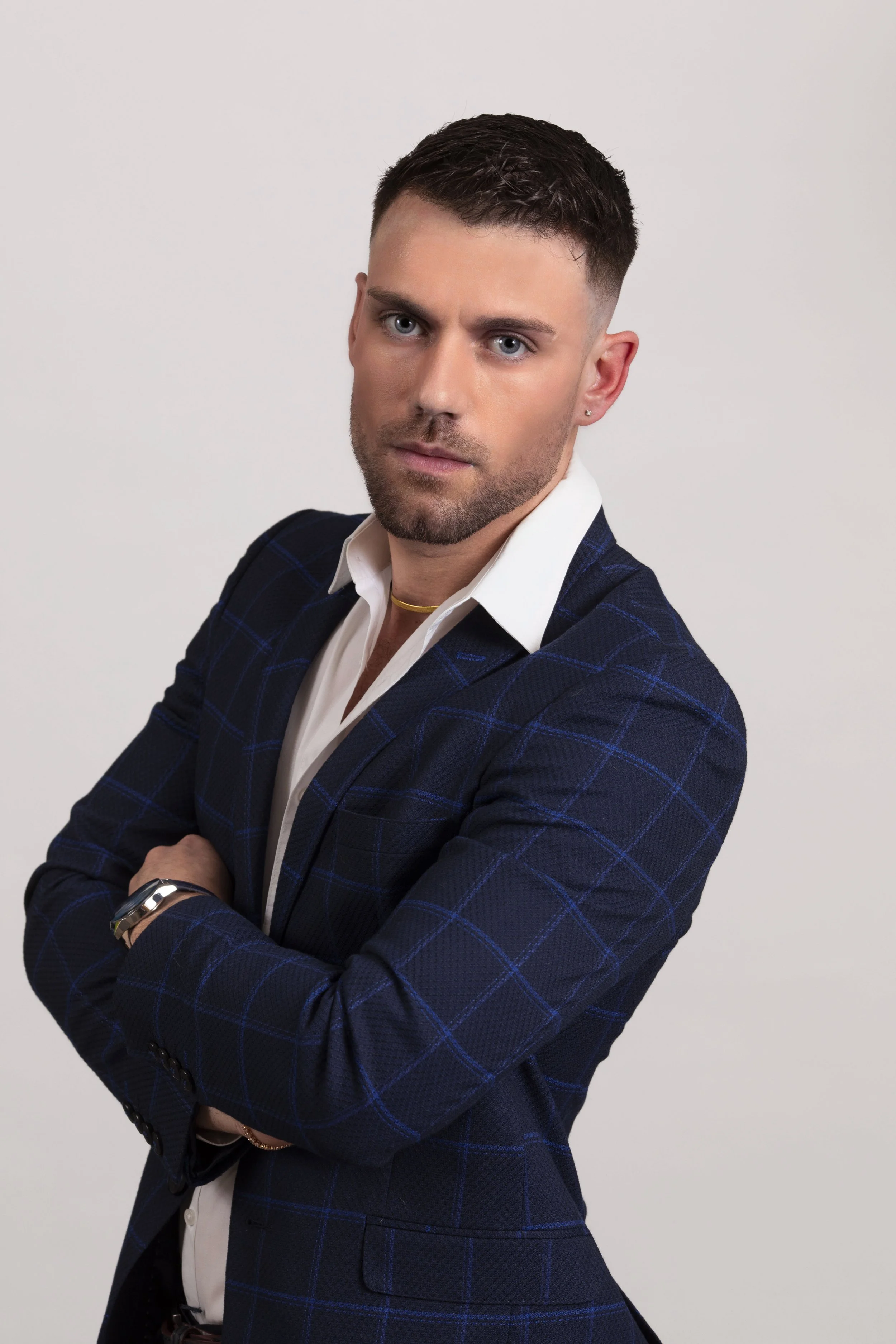 Ritratto di un uomo con capelli corti, indossa una giacca blu a quadri e una camicia bianca, con braccia incrociate, fronte frontale, sfondo bianco.