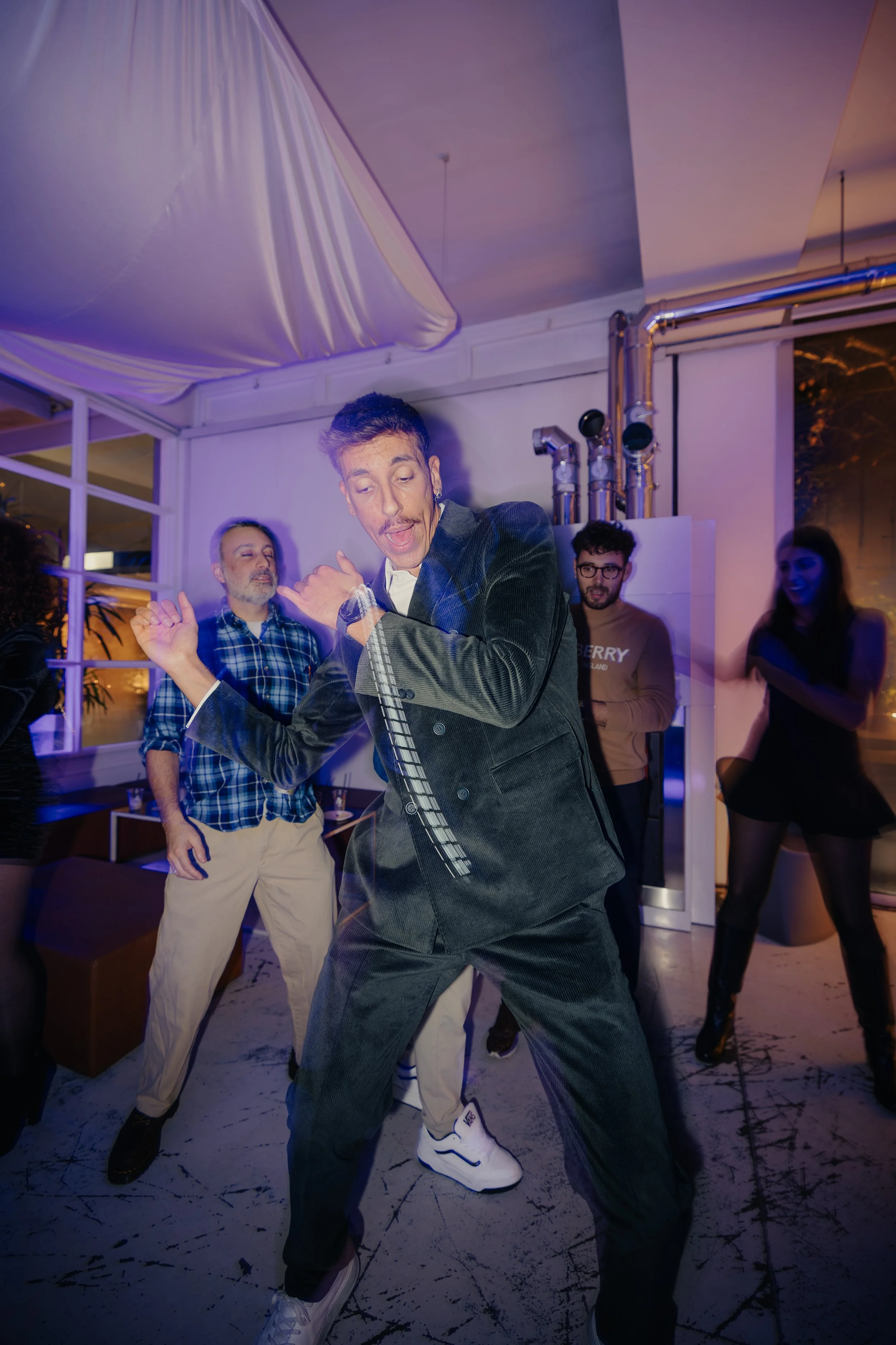 Gruppo di persone che ballano e si divertono in una festa in ambientazione moderna con luci colorate e atmosfera vivace.