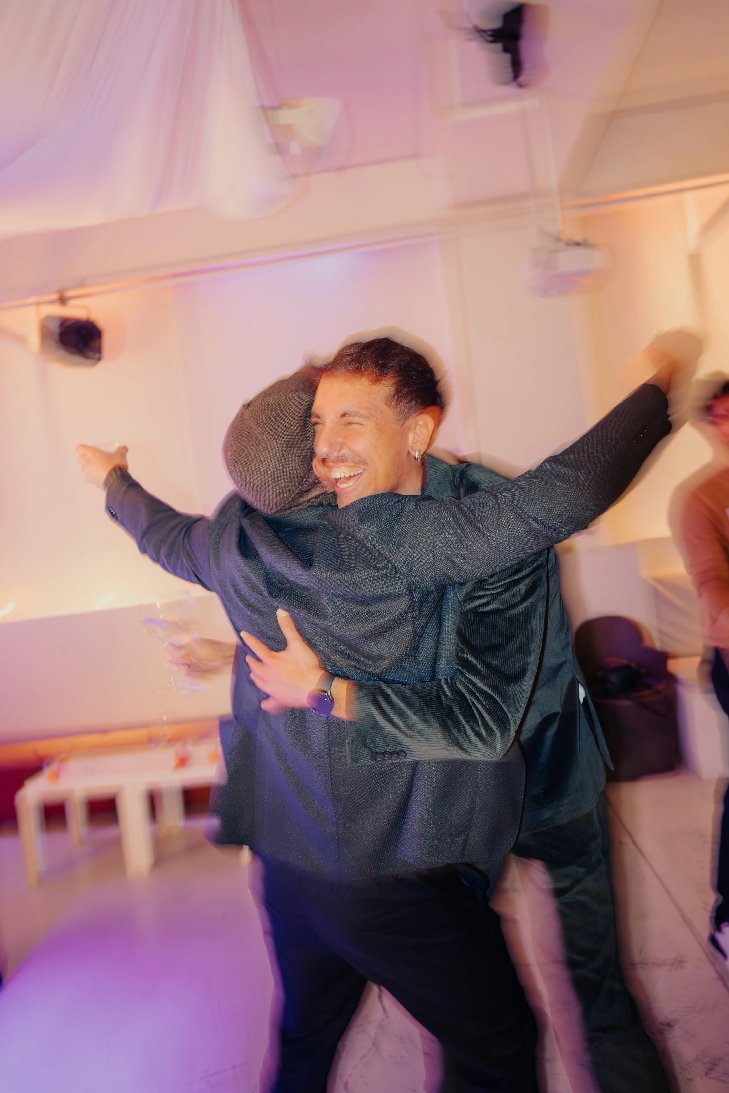 Due persone che si abbracciano e sorridono durante una festa in un ambiente interno decorato con luci calde.