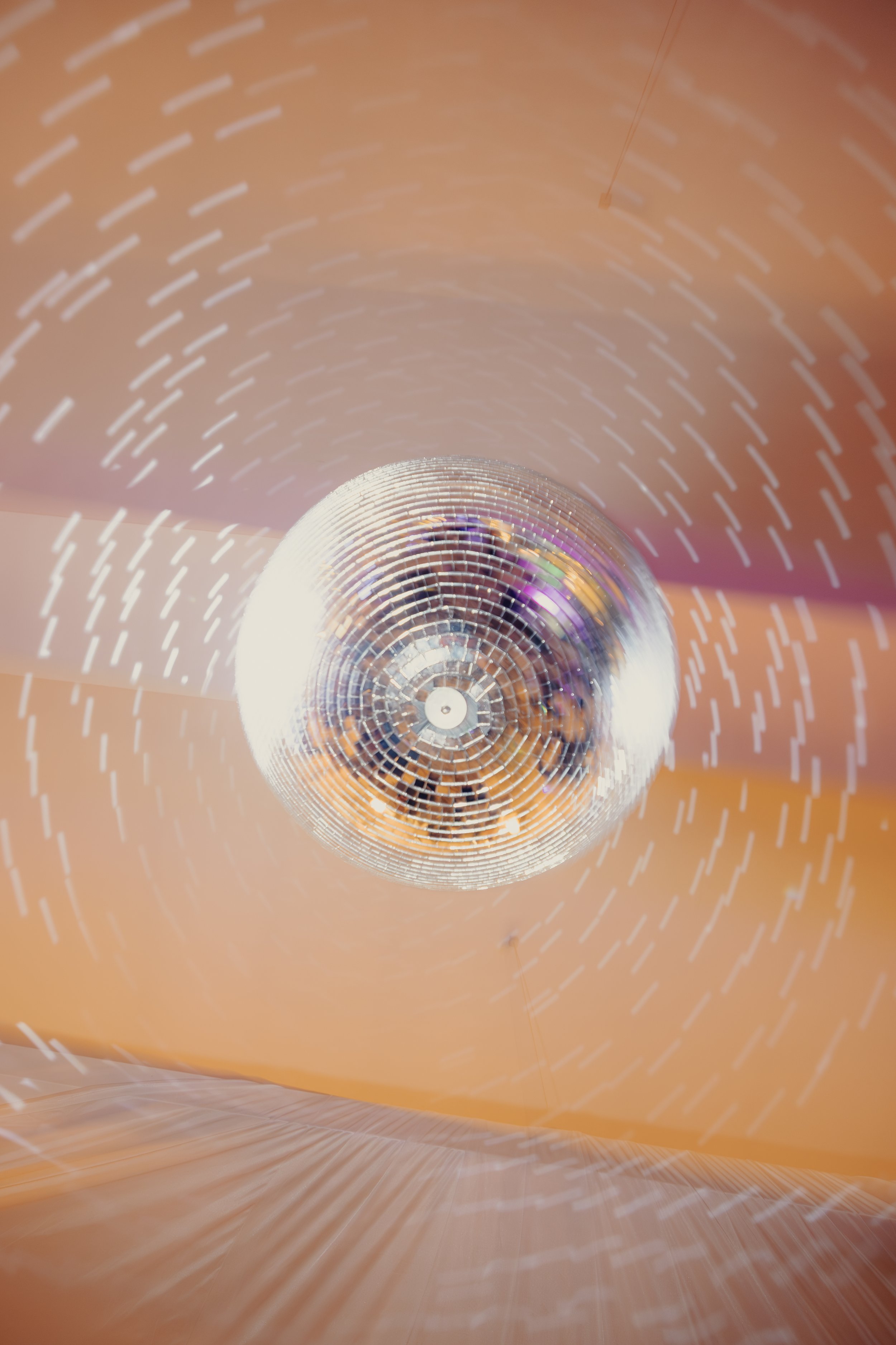 Un grande specchio a forma di palla disco che riflette le luci e le persone in una stanza con pareti arancioni.
