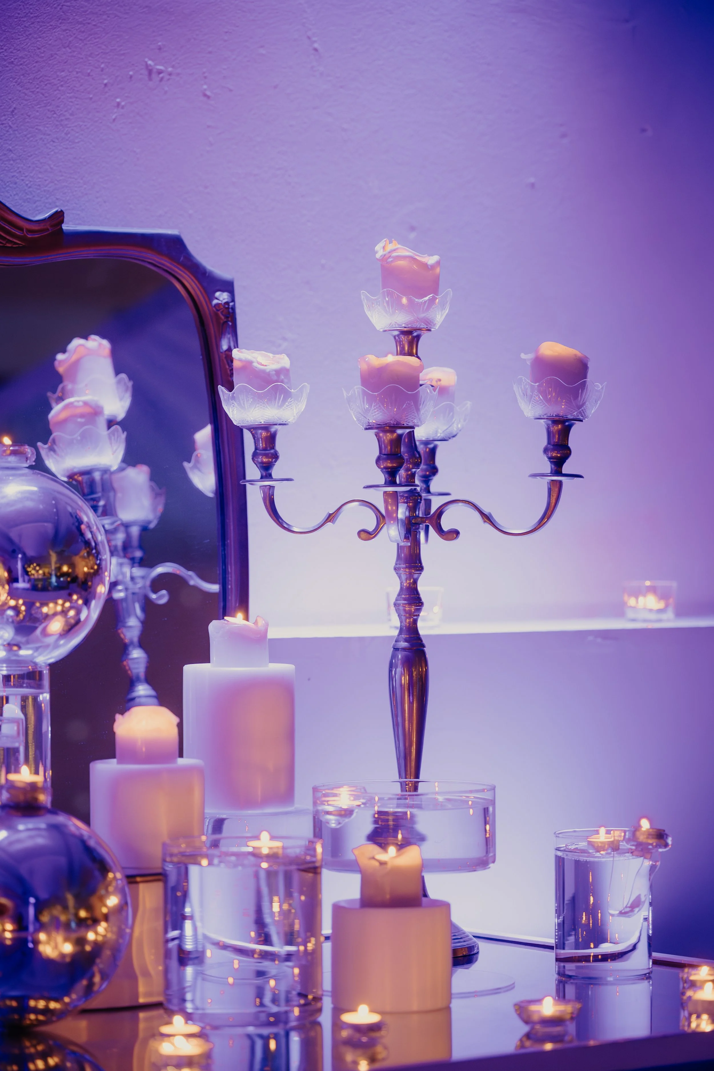 Candeliere d'argento con sei candele accese, circondato da varie candele bianche e tealight, con specchi e decorazioni decorative con luci calde e riflessi