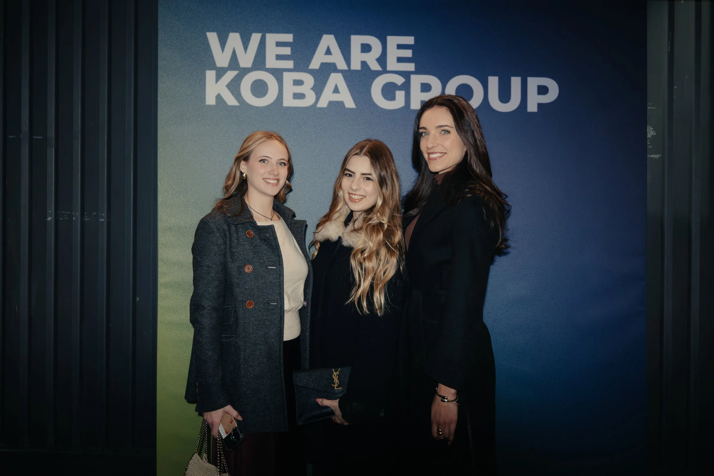 Tre donne sorridenti davanti a un esempio di logo della KOBA Group.