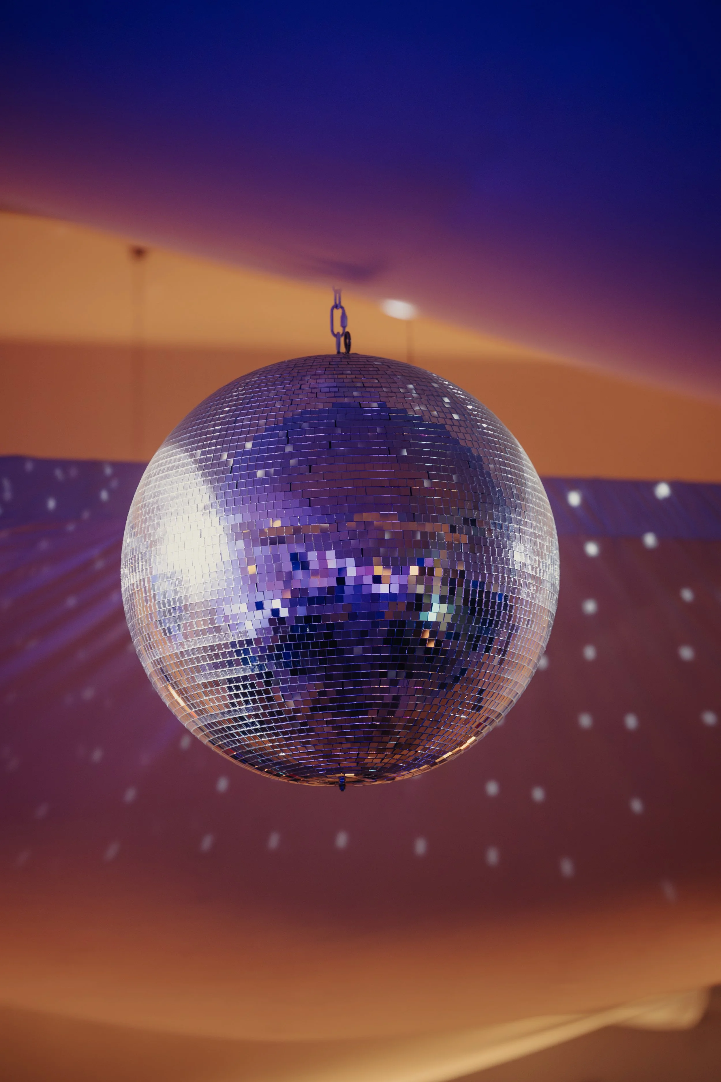 Palla disco riflettente appesa al soffitto con luci colorate che proiettano piccoli punti di luce sulle pareti sottostanti.