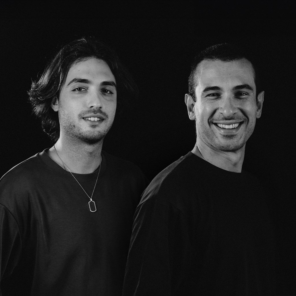 Due uomini sorridenti posano contro uno sfondo nero.