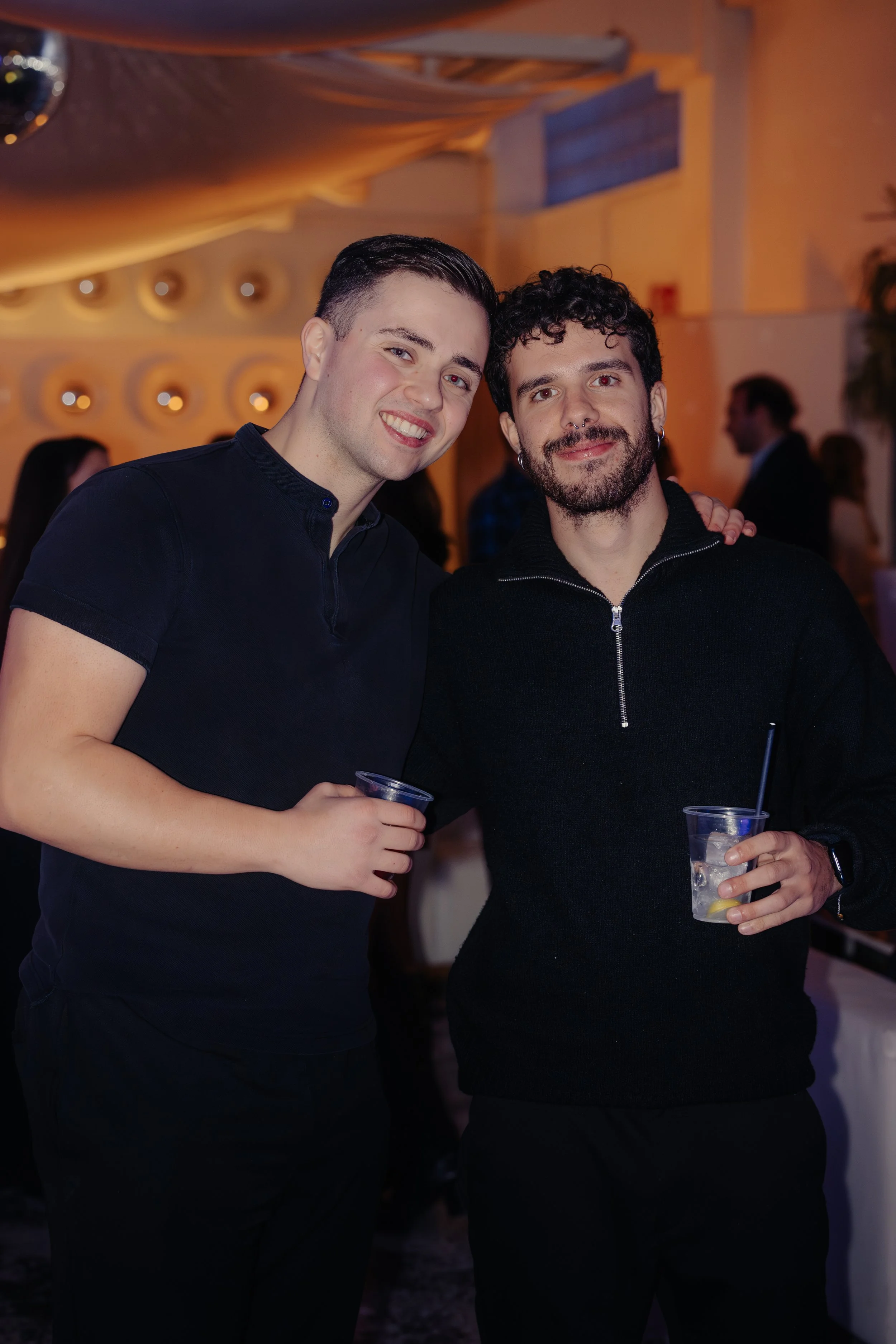 Due uomini sorridenti che brindano, uno con una bevanda al limone in un ambiente festoso.