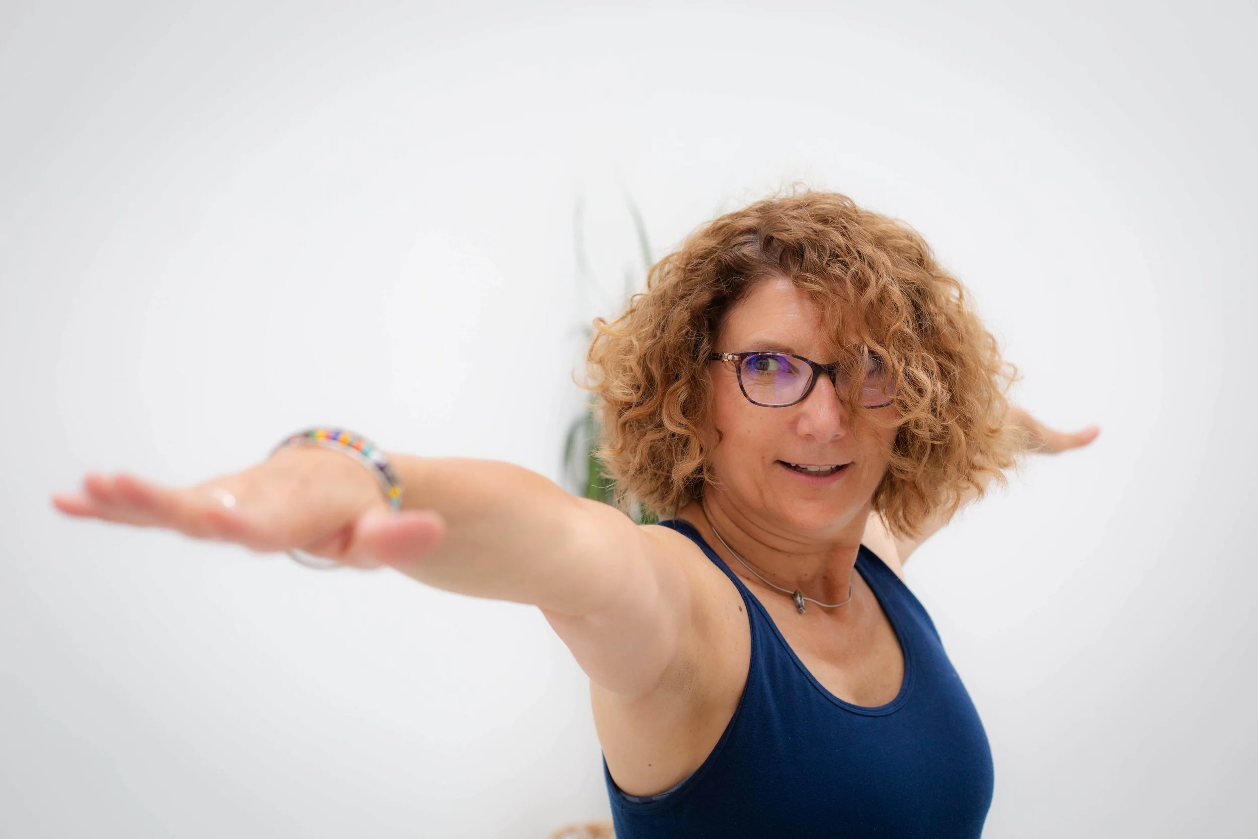 Woman with curly hair and glasses doing a yoga pose, wearing a blue tank top.