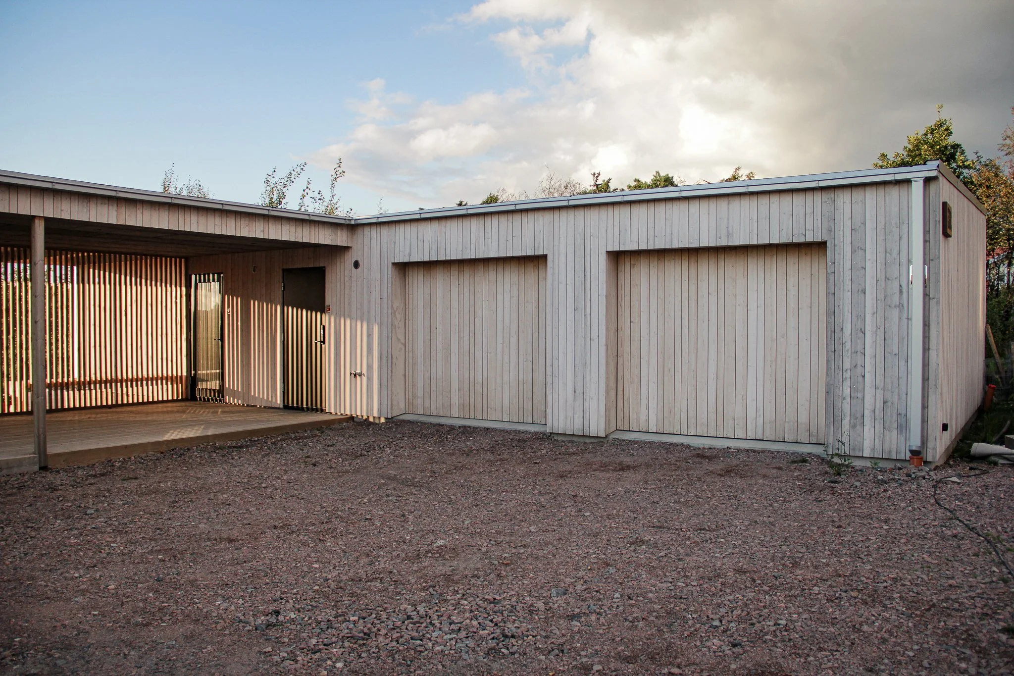 Träbyggnad med garageportar och uppfart på grus.