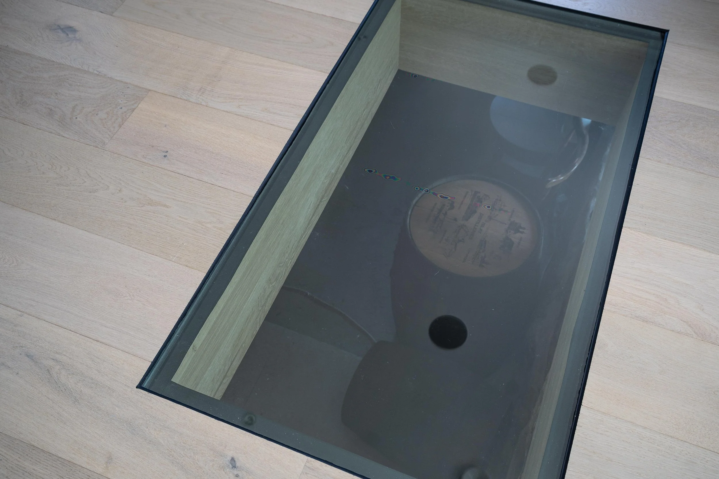 Glaslucka i golvet, med öppen utrymme under, träpaneler på golvet. O Lind AB.