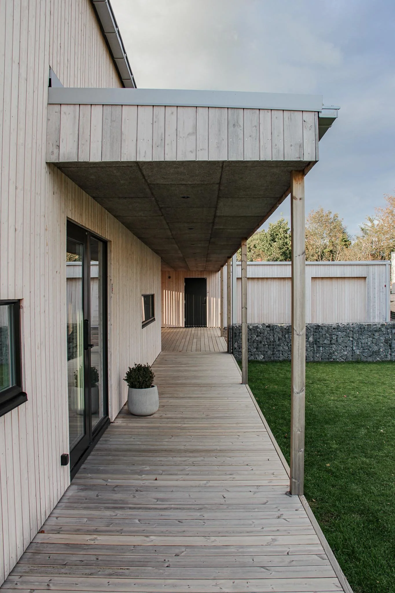 Modernt hus med träfasad och altan, planteringskruka, gräsmatta och träd.