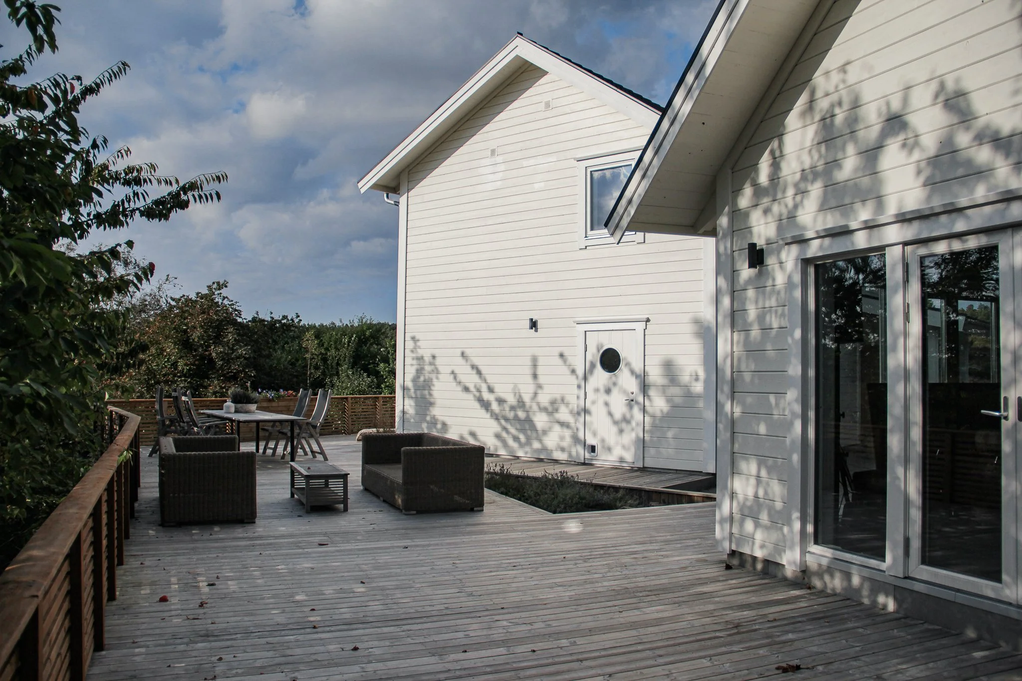 Vit villa med trädäck och trädgårdsmöbler under en molnig himmel.