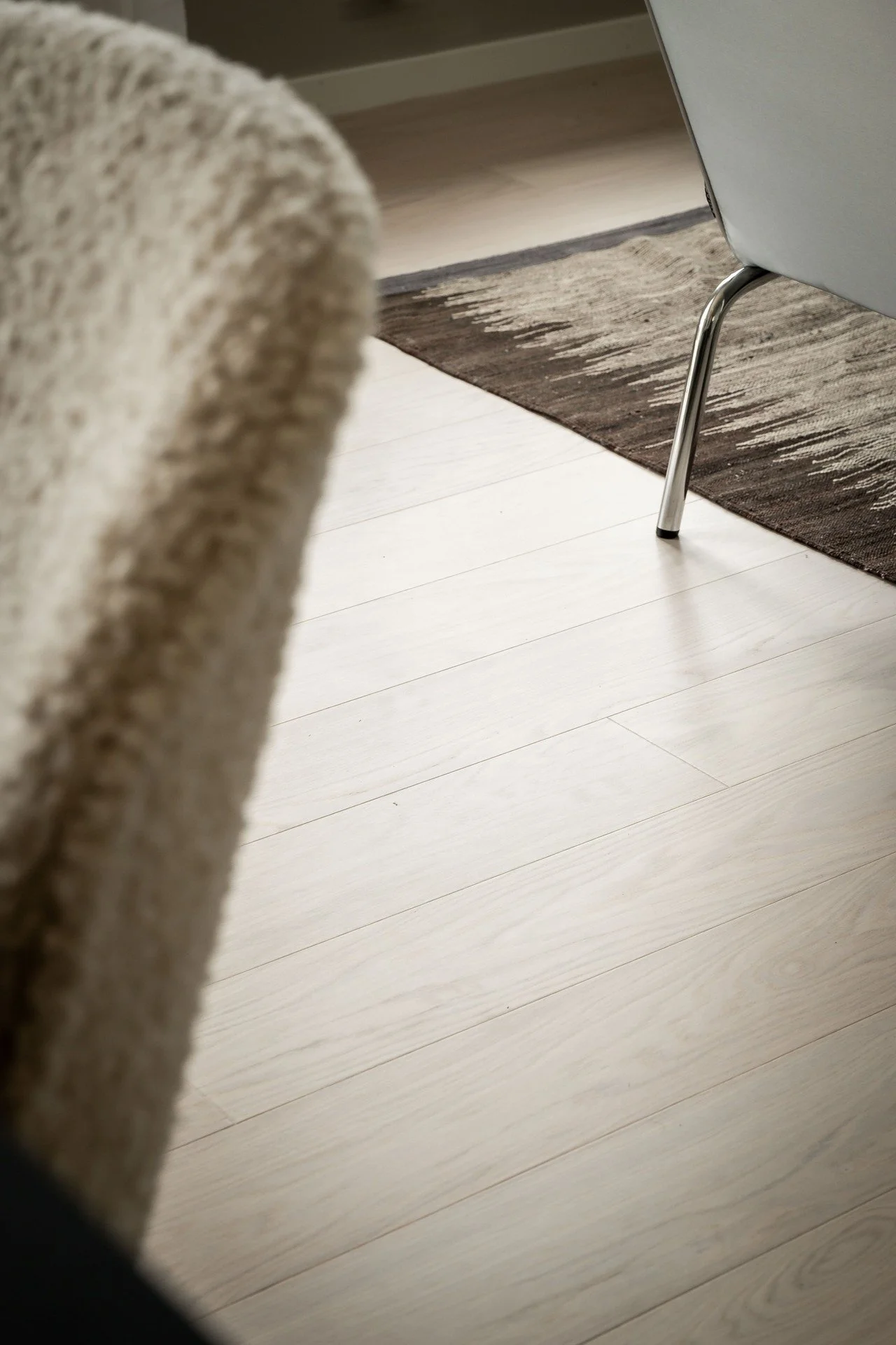 Interiör med beige stol, mörk matta och ljust trägolv. O Lind AB.