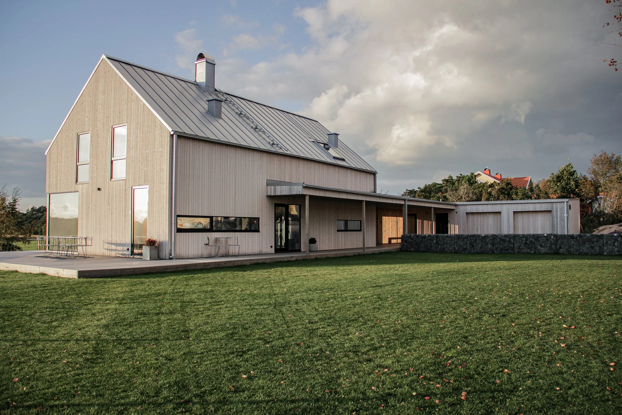 Modernt trähus med metalltak och stora fönster på en välskött gräsmatta under molnig himmel.