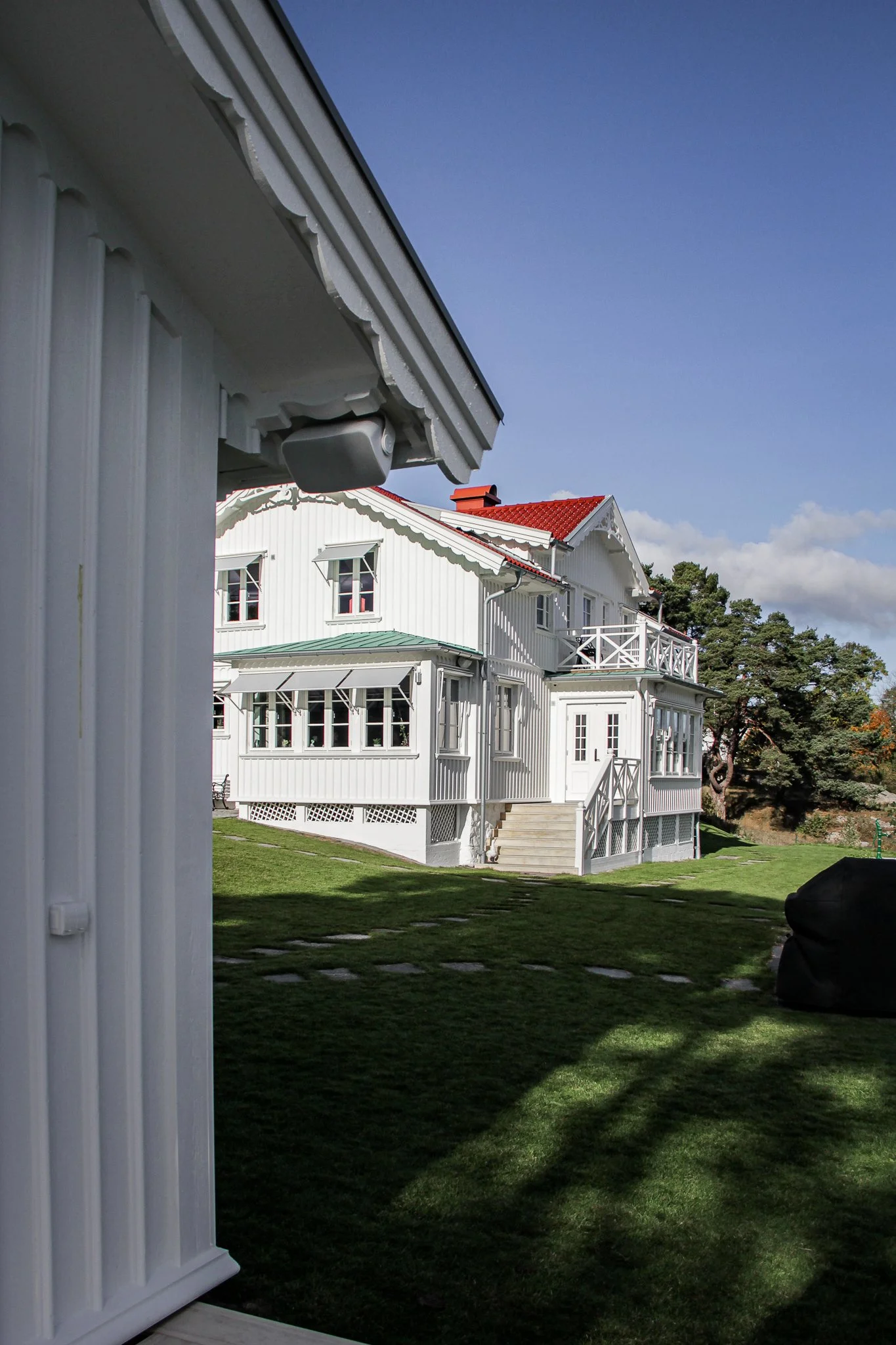 Vit villa med röda tak, grön gräsmatta, ljusblå himmel i bakgrunden.