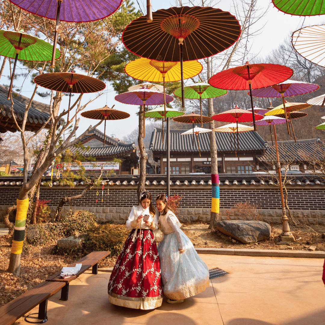 Visitors wearing traditional hanbok beneath a colourful umbrella display in South Korea.