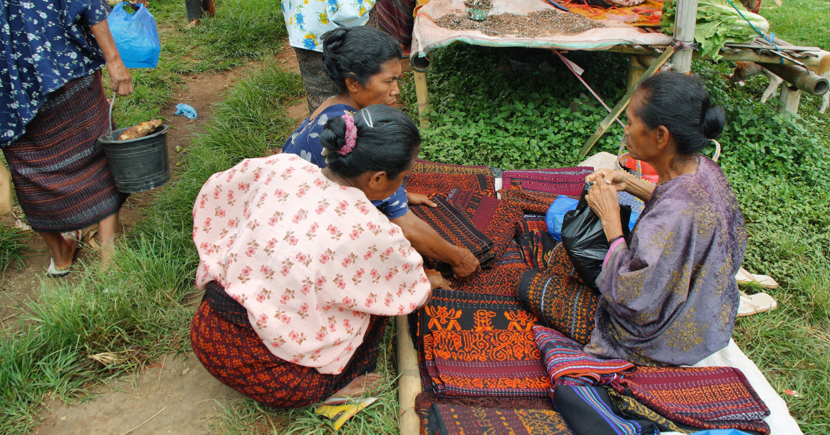 Women examining patterned ikat textiles at a local market in Flores