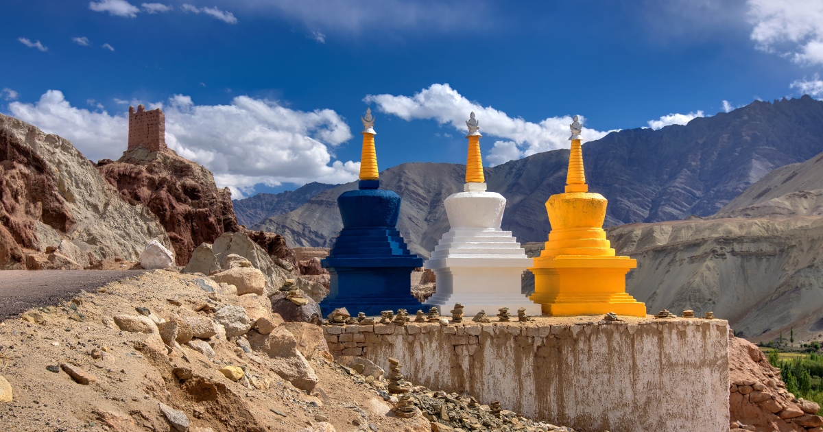 Three colourful Buddhist chortens beside a road in Ladakh with barren mountains behind them.