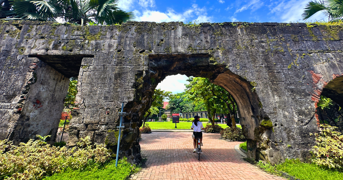 Cyclist passing through a historic stone arch in Intramuros, Manila