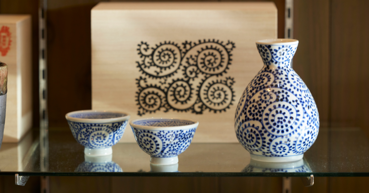 Tobe-yaki porcelain vase and cups with indigo blue spiral patterns on a white ground displayed on a shelf.