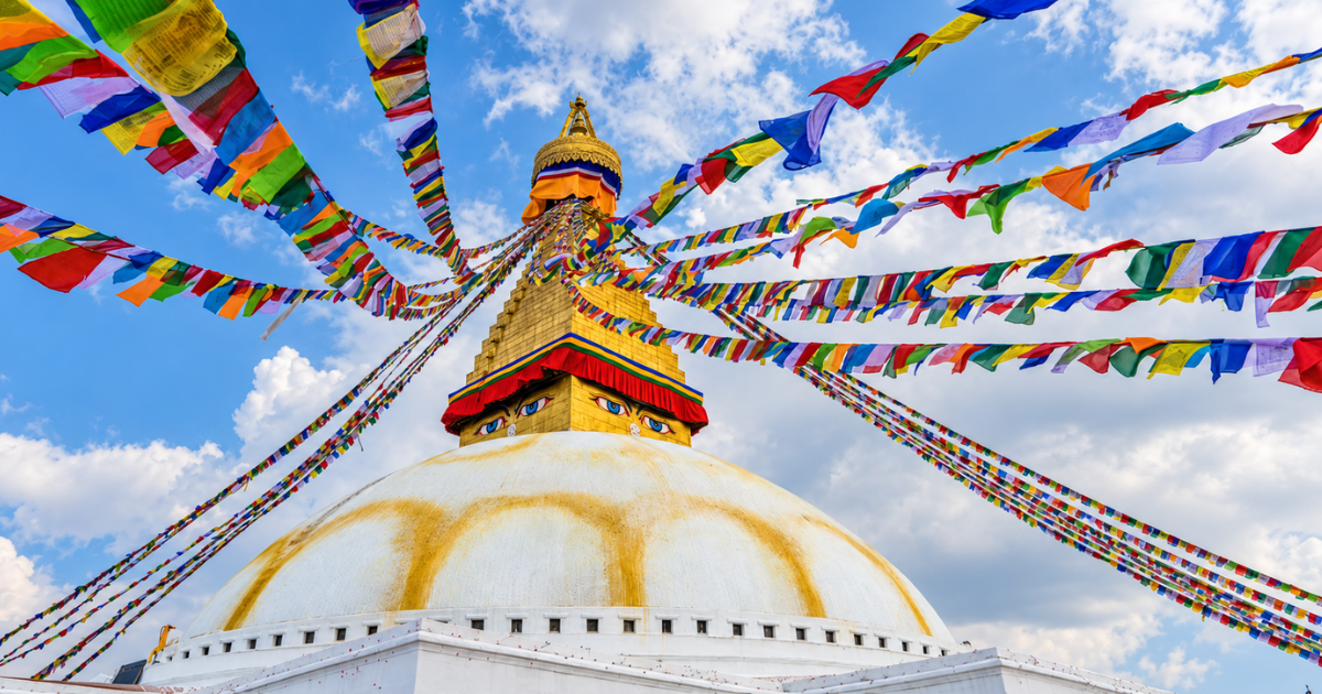 Boudhanath Stupa in Kathmandu, with colourful Tibetan prayer flags stretching above its white dome and gilded spire.