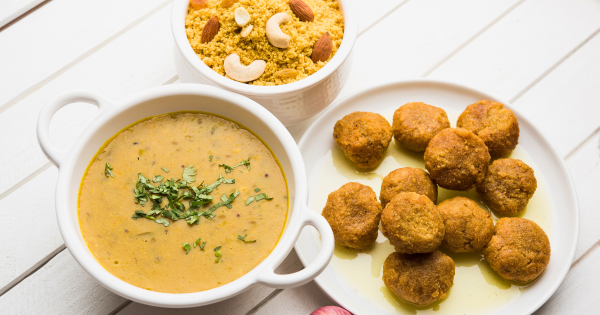 Bowl of dal, plate of ghee-soaked baati and a bowl of churma topped with cashews and almonds