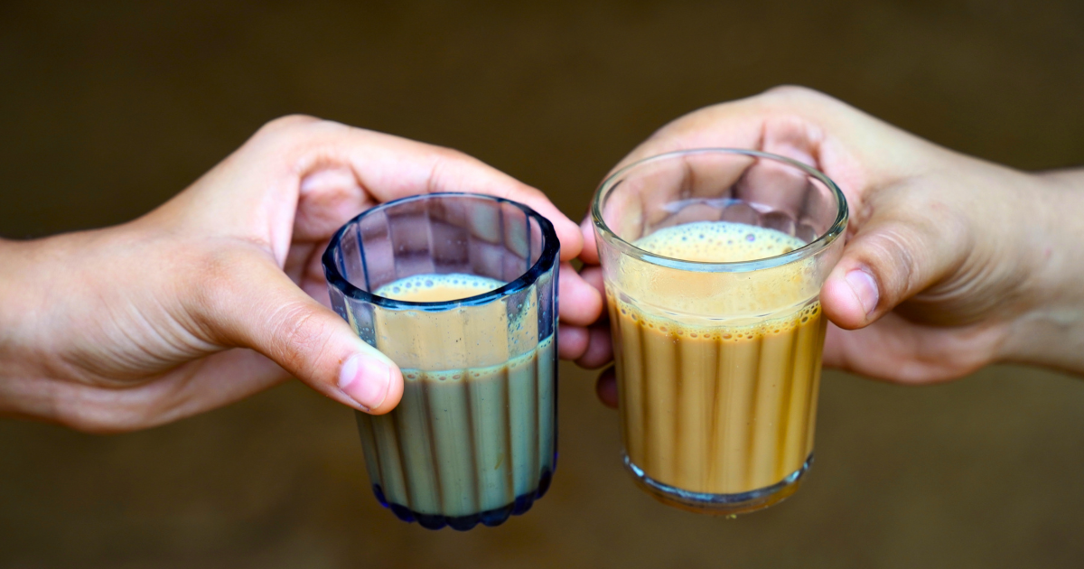 Two glasses of masala chai held in mid-air as they are clinked together