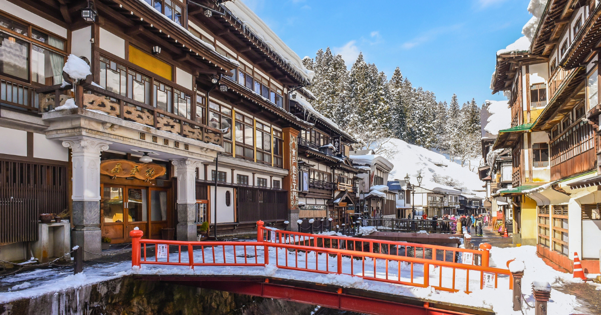 A narrow street of traditional wooden ryokan buildings lined either side of a small river