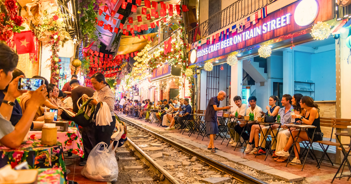 People sitting at cafes and bars along Hanoi's Train Street at night with railway tracks running between the tables