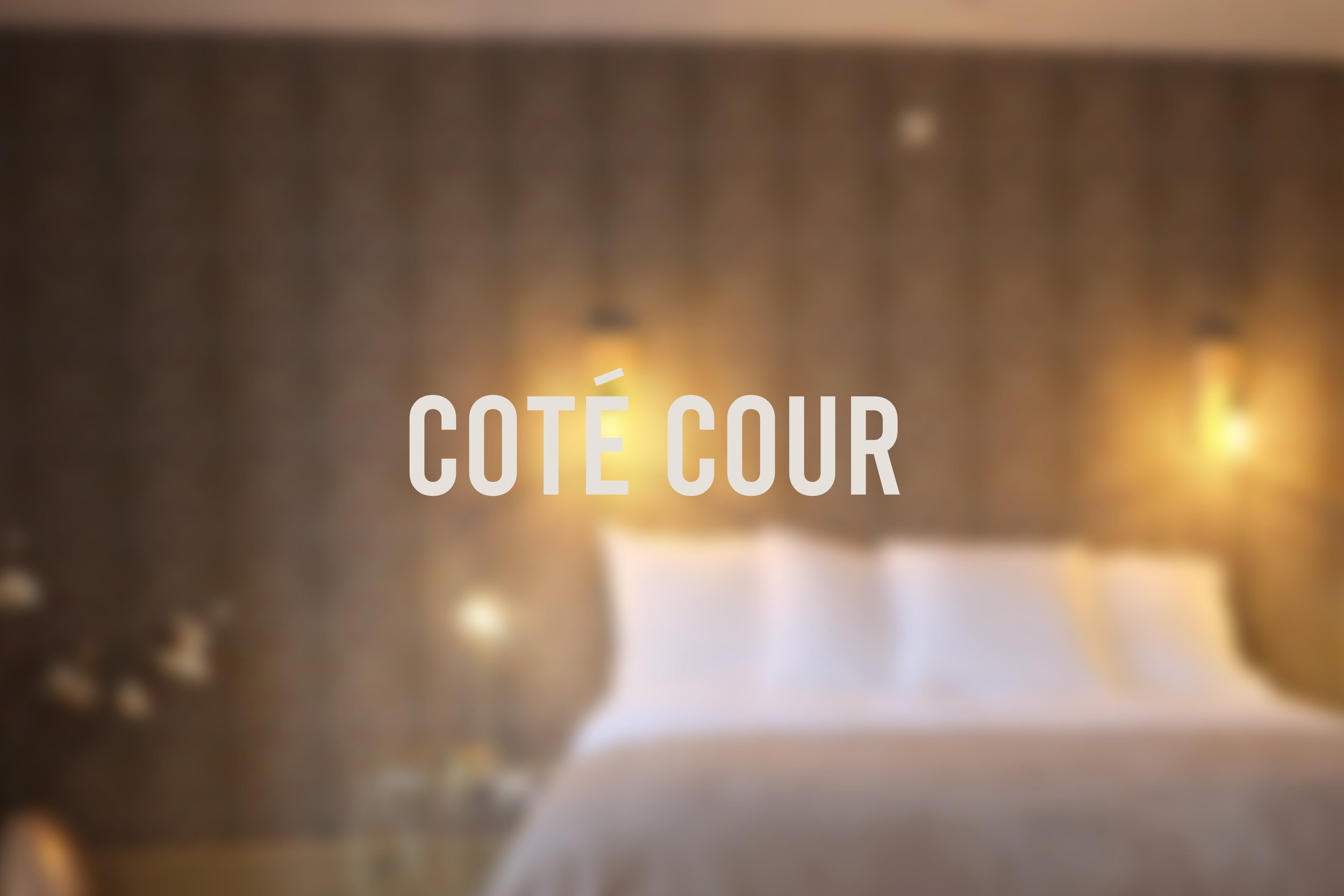 Une vue floue d'une chambre avec un lit et deux lampes murales, avec le texte 'Côté cour' en premier plan.