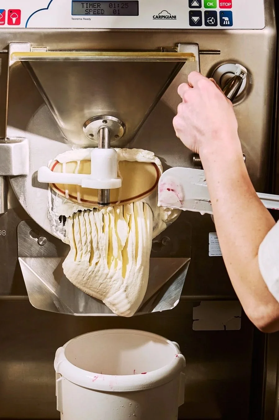 Spouse Studio. Gemma Tree. A person using an industrial gelato or ice cream machine to make ice cream, with a large cone of soft ice cream being extruded into a container below.