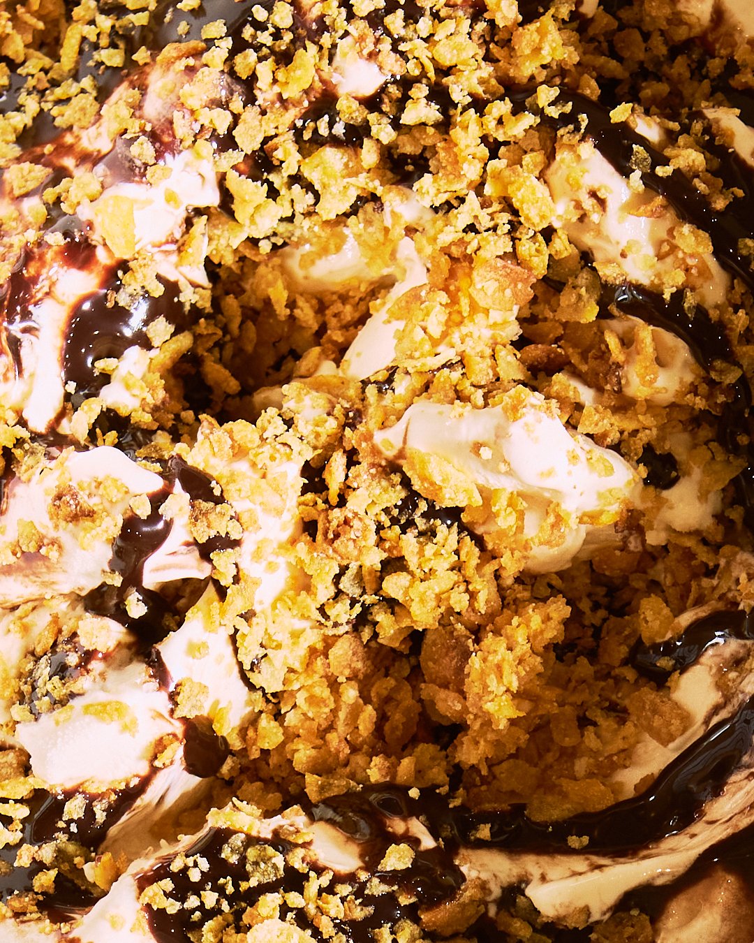 Spouse Studio. Gemma Tree. Close-up of a dessert with crumbled topping, vanilla ice cream, chocolate syrup, and cookie pieces.