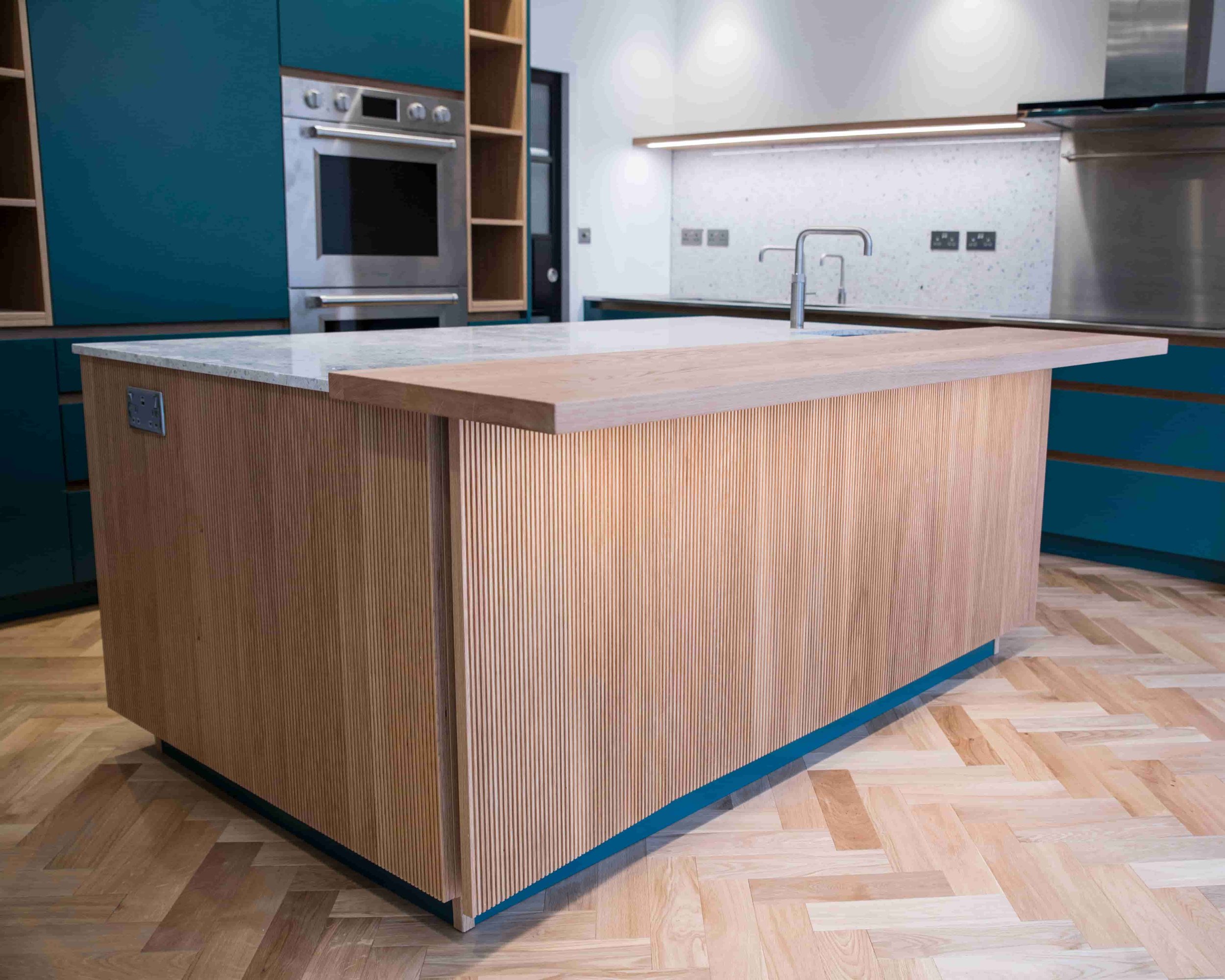 Bespoke kitchen renovation featuring a fluted oak island, quartz worktops, herringbone timber flooring and contemporary cabinetry completed by Ash Technical Services.
