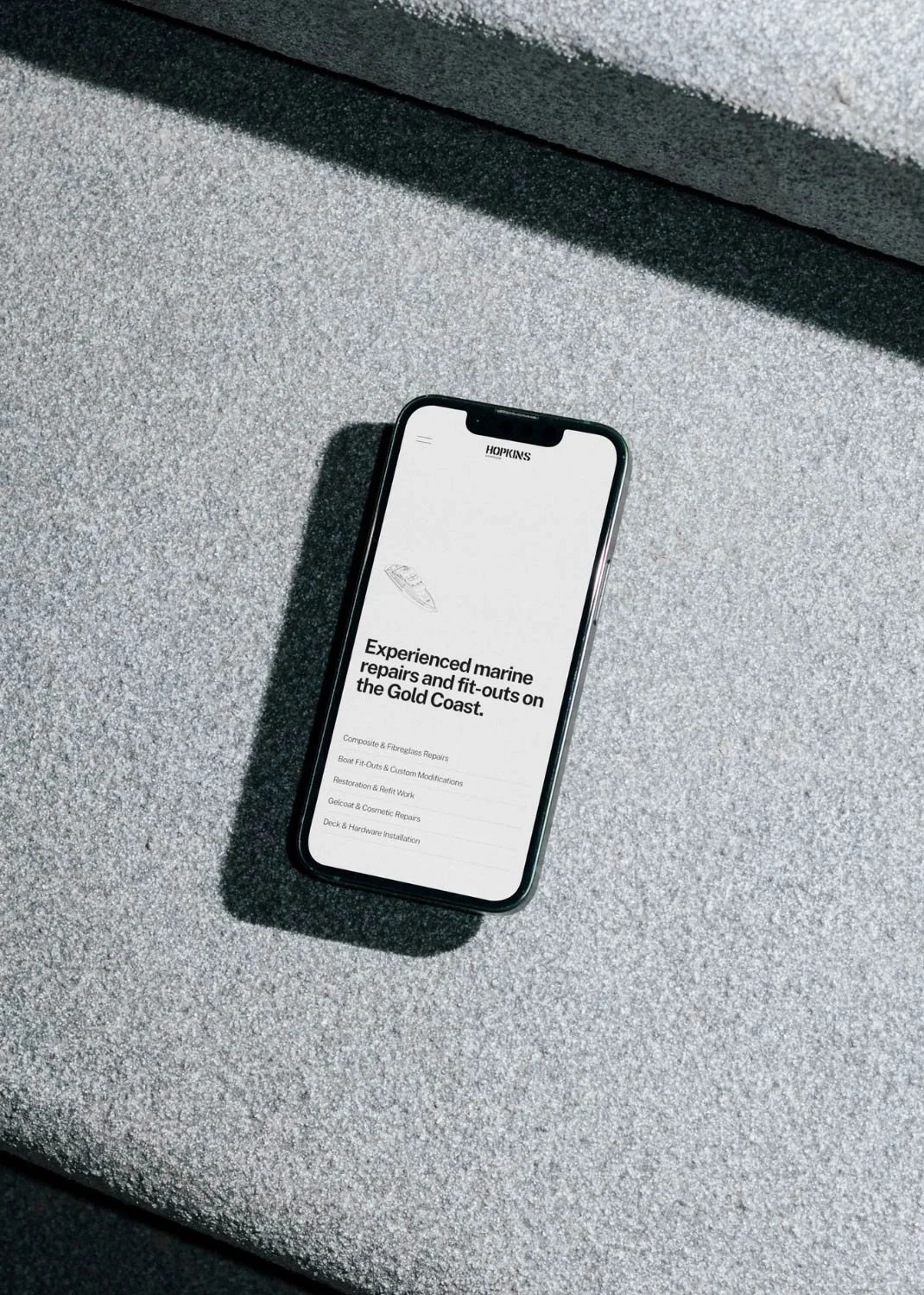 A smartphone on a gray textured surface displaying a webpage for marine repairs and fit-outs on the Gold Coast.