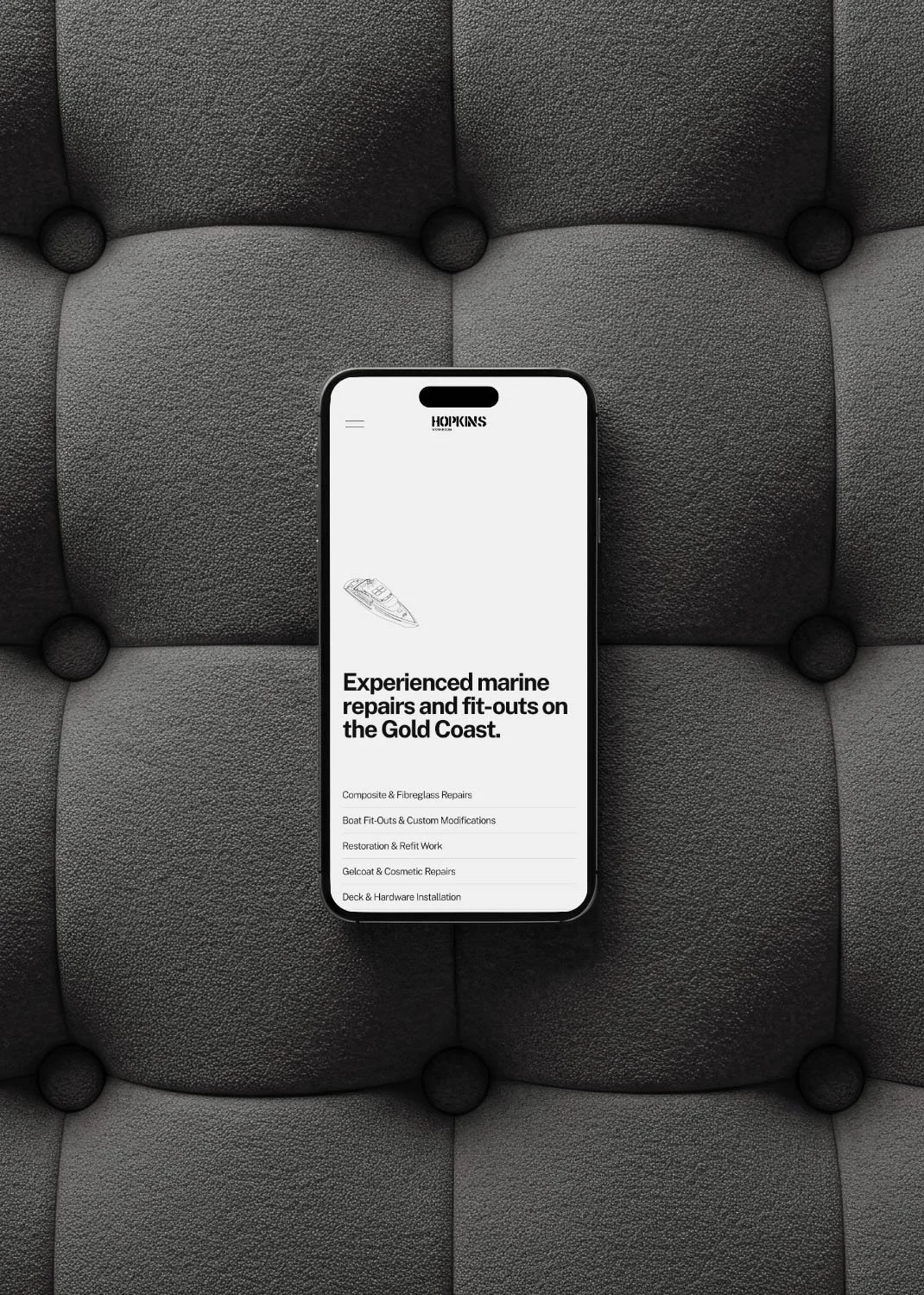 A smartphone displaying a marine repair service website on a dark gray, quilted surface.
