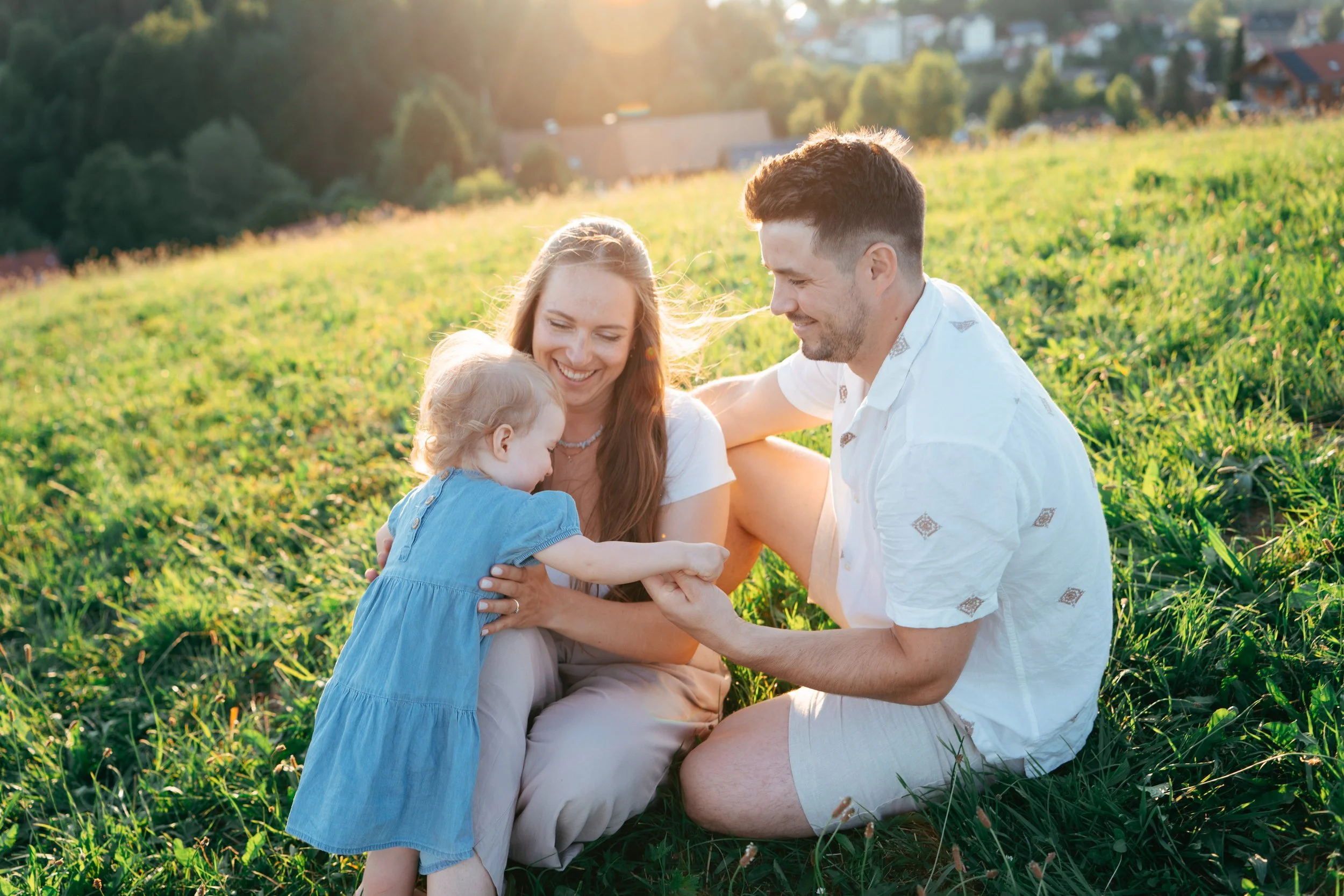 Familie mit kleinem Kind sitzt auf einer Wiese im Sonnenschein und spielt miteinander.