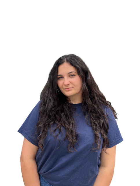 A young woman with long, wavy dark hair and a slight smile, wearing a blue t-shirt, standing against a white background.