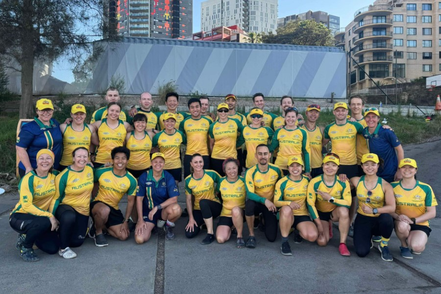 The Premier Australian Dragon Boat Team, a group of women and men dressed in green and gold Australian sports uniforms, some wearing caps, posing outdoors on a boat ramp.