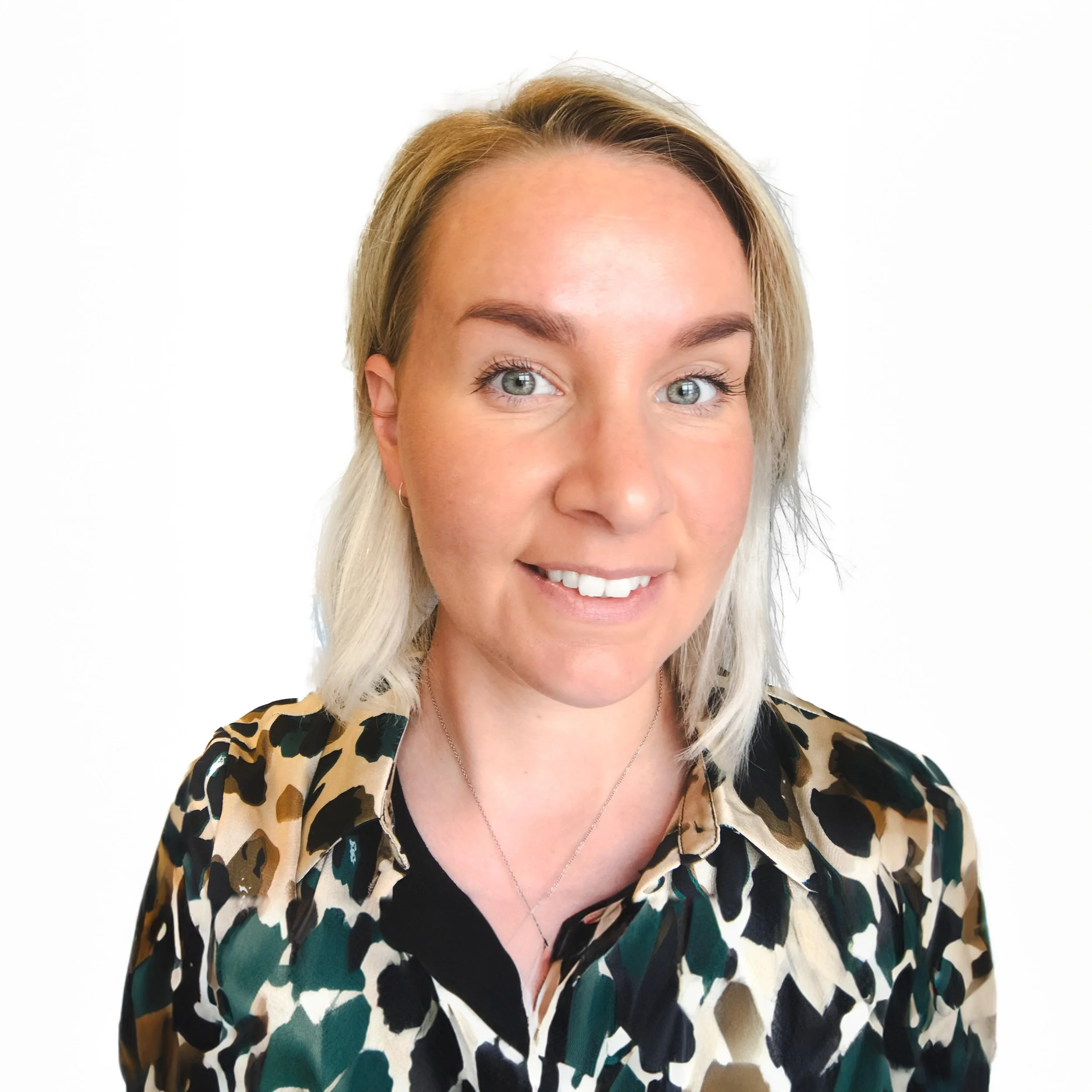 Porträtt av en kvinna med blont hår, ljus hud och blå ögon, som bär en leopardmönstrad blus och ett silverhalsband, mot en vit bakgrund.