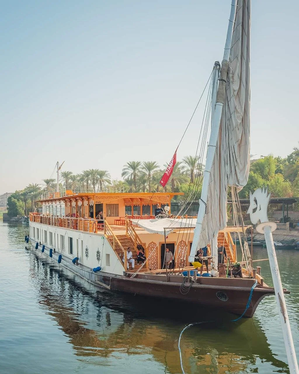 A traditional wooden boat cruising on a river with palm trees and lush greenery in the background.