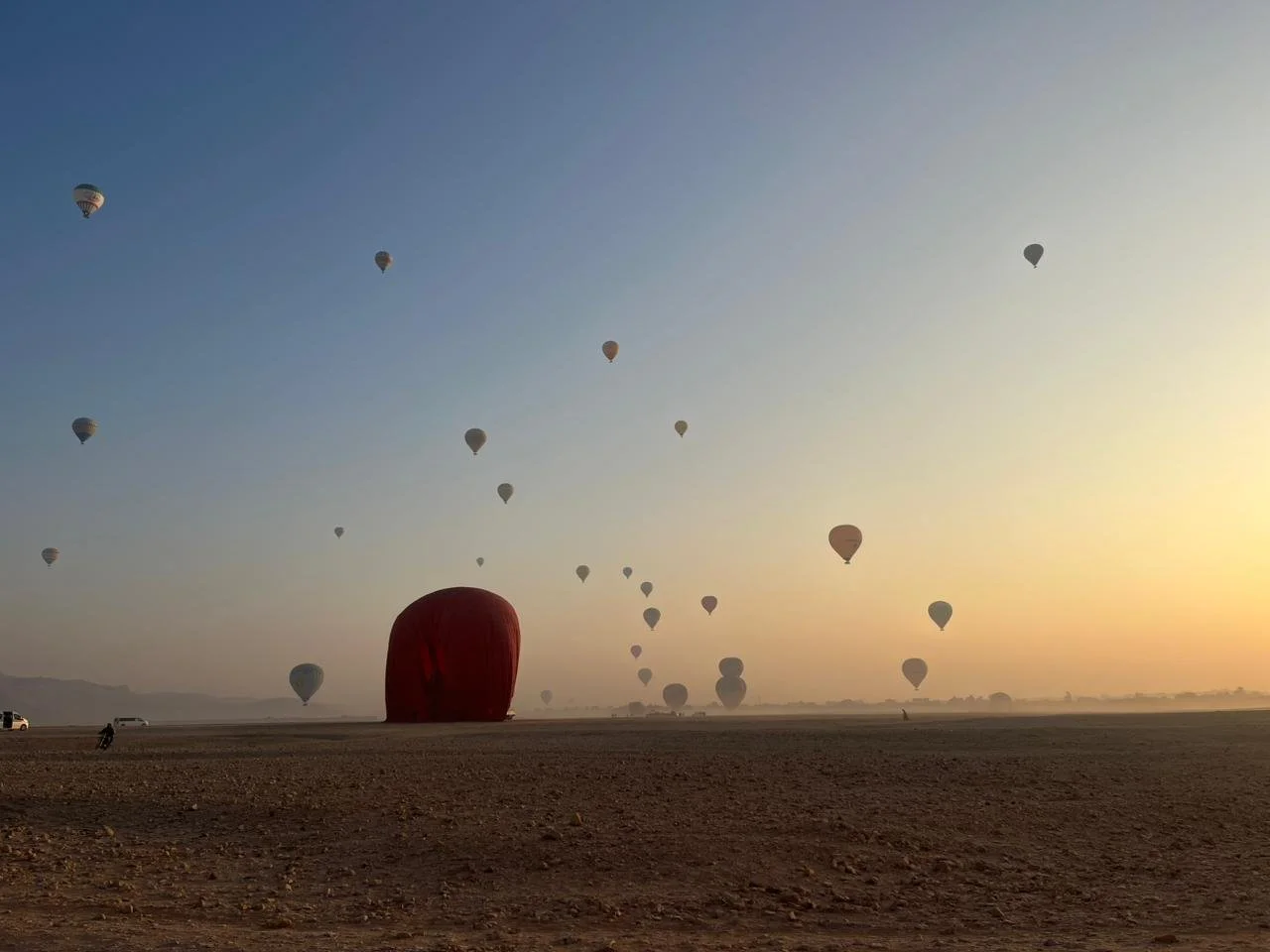 Numerous hot air balloons floating in the sky during sunset over a flat, open landscape.