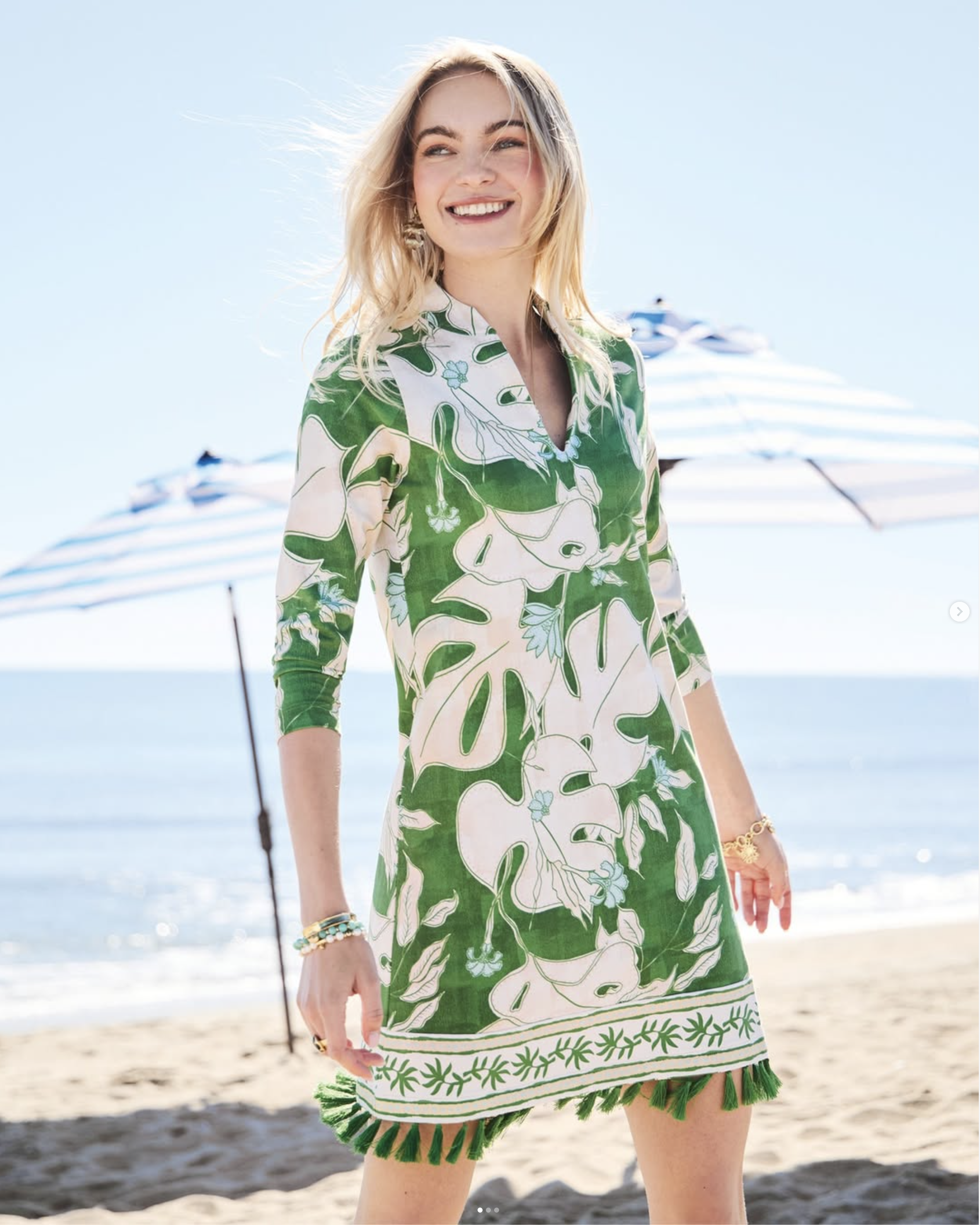 Woman wearing a green floral dress on a beach with blue striped umbrellas in the background