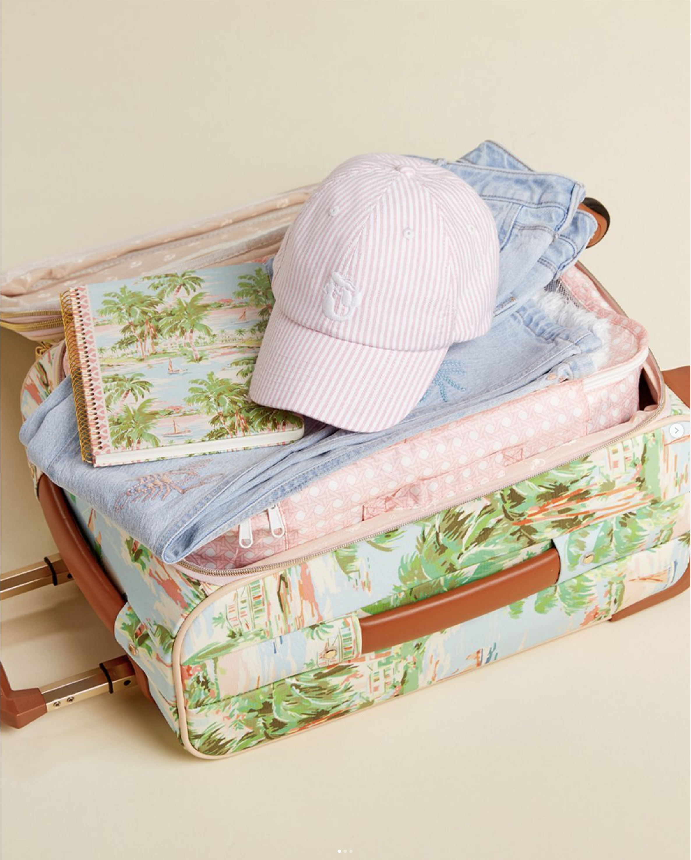 Open floral-print suitcase with pink cap, notebook, and folded clothes.