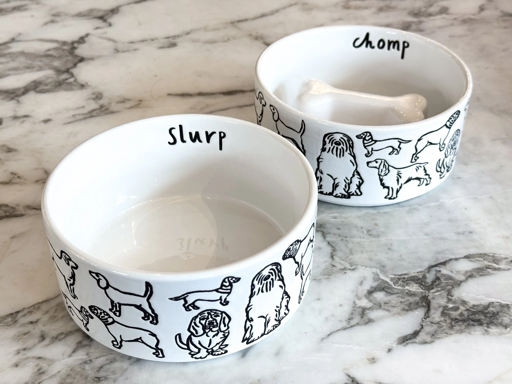 Two white ceramic bowls with black dog illustrations and labels for different dog traits, placed on a marble surface.