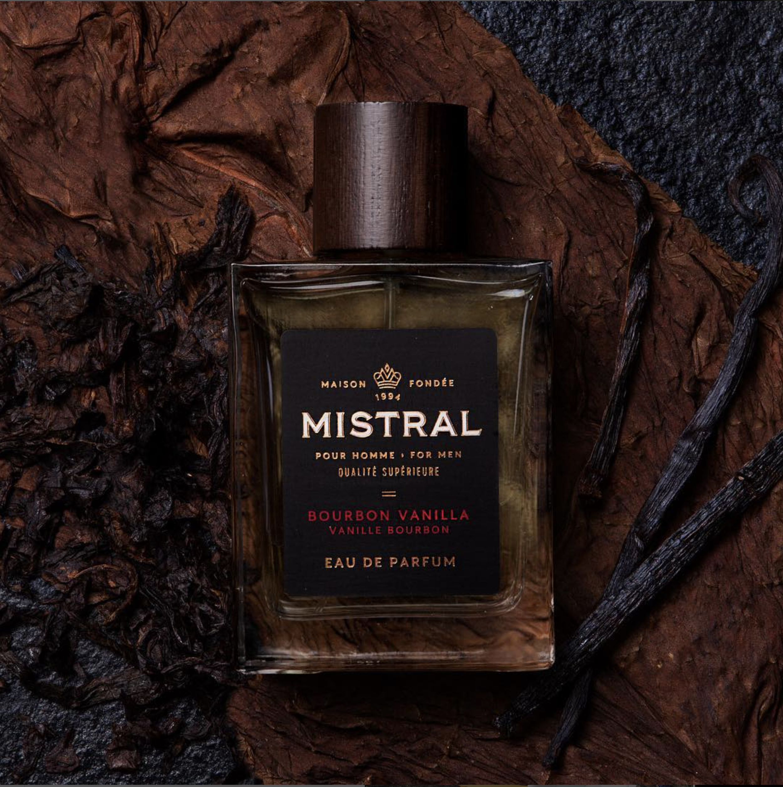 Mistral bourbon vanilla men's eau de parfum bottle with vanilla beans and textured brown surface.
