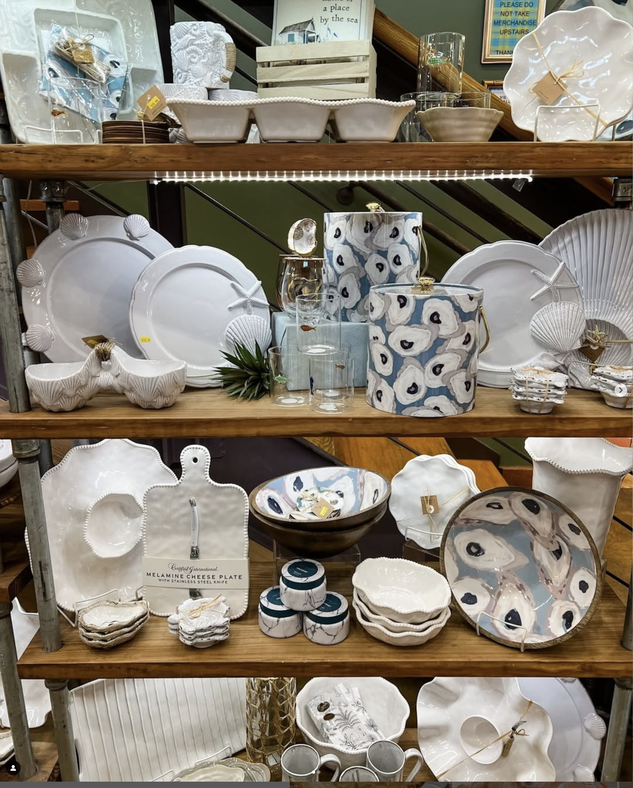 Display of kitchenware with white plates, decorative bowls, glassware, and patterned ceramic pieces on wooden shelves.