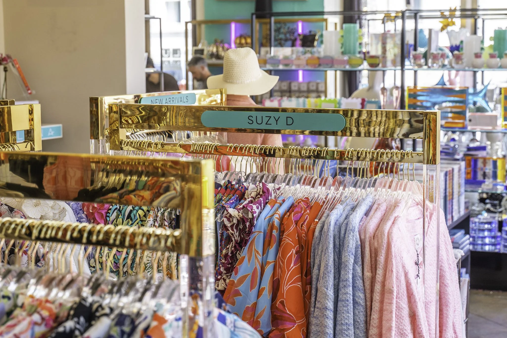 Clothing rack in a store with colorful dresses and shirts, and signs labeled 'New Arrivals' and 'Suzy D'.