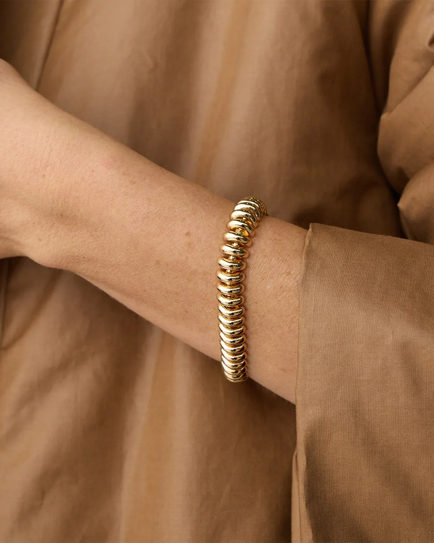 Close-up of a person's wrist wearing a gold bracelet against a beige-brown fabric background.