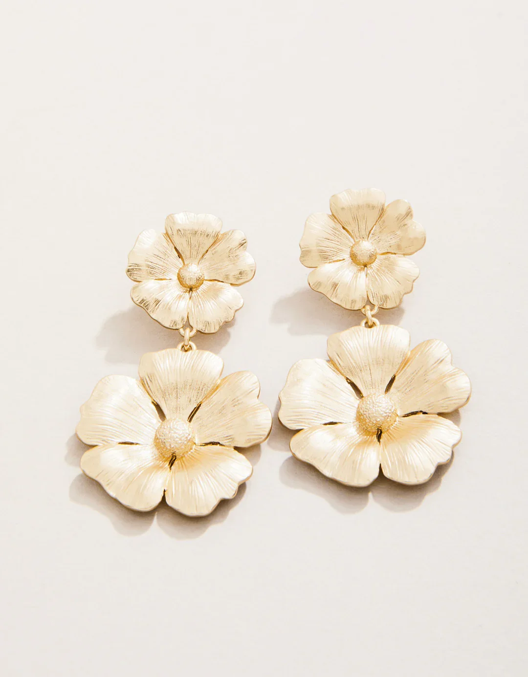 Pair of cream-colored floral earrings with two flower-shaped elements hanging below each other.