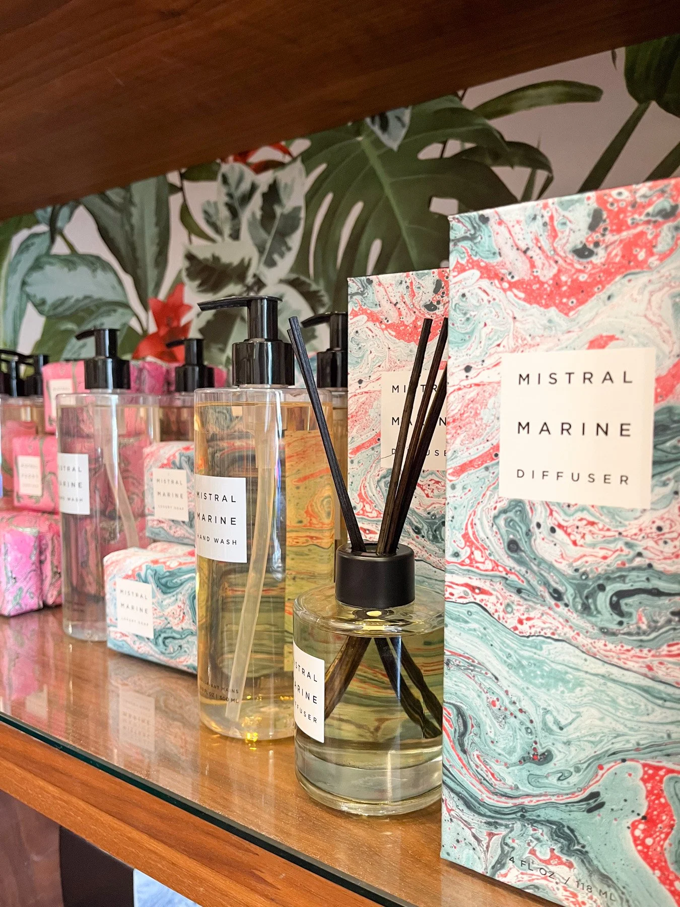 Display of Mistral Marine scented products, including hand wash, diffuser, and soap, with colorful marbled packaging on a wooden shelf.